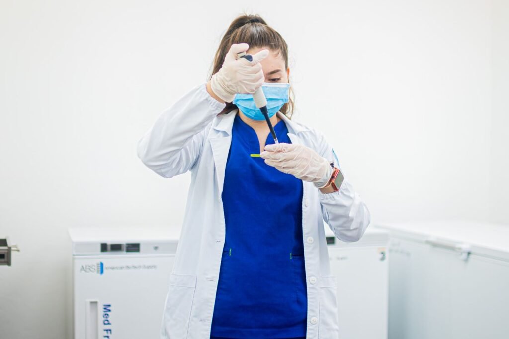Female healthcare professional using a pipette in a laboratory setting, wearing protective gear.